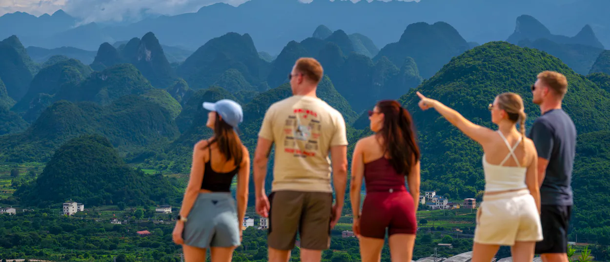 Travellers look out from a hilltop over a sea of jagged green limestone peaks under a blue sky.