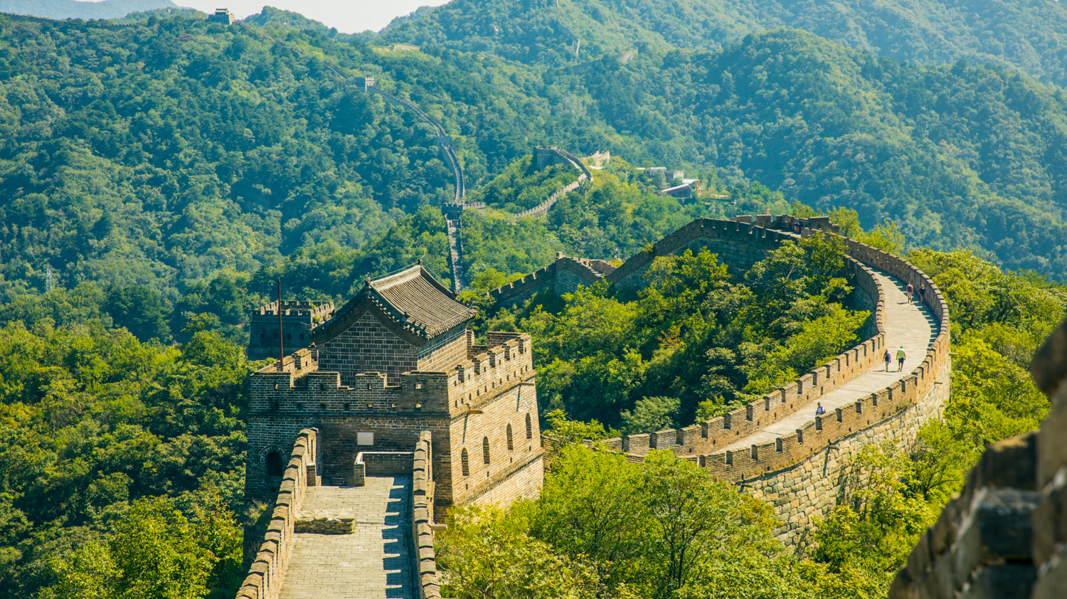 Ancient stone Great Wall of China with watchtowers snaking across forested mountain ridges.