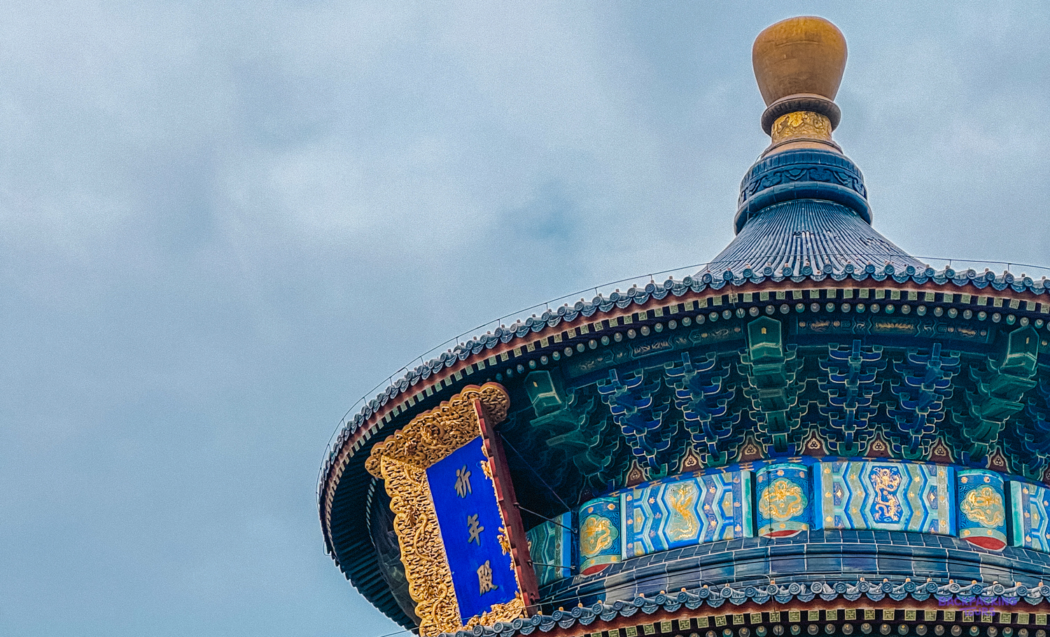 Intricate blue and gold roof details of a historic Chinese temple in Beijing under a cloudy sky.