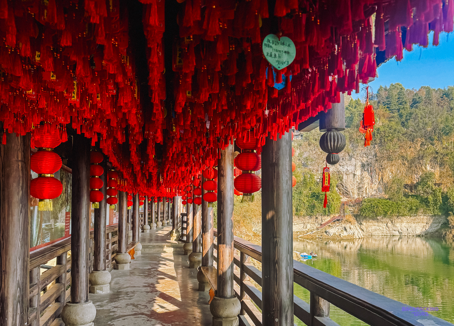 A traditional wooden walkway adorned with hundreds of red lanterns, overlooking a river in Furong Ancient Town.
