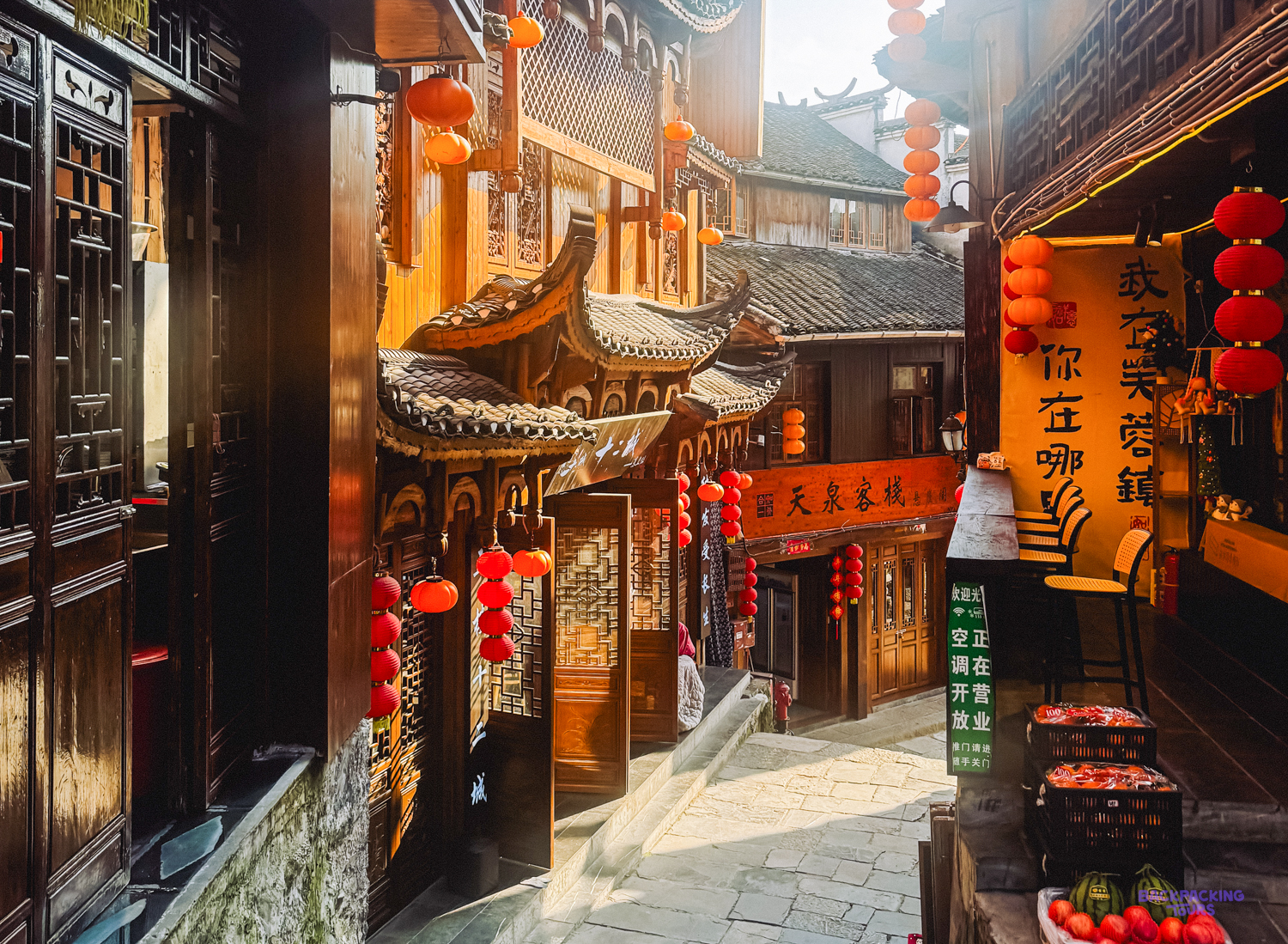 Sunlight illuminates a traditional street in Furong Ancient Town, adorned with wooden buildings and red lanterns.