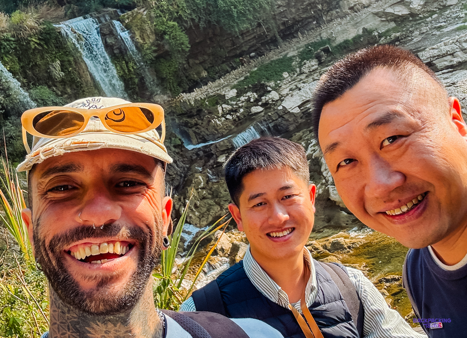 Smiling travelers capture a selfie with a cascading waterfall backdrop in Furong Ancient Town.