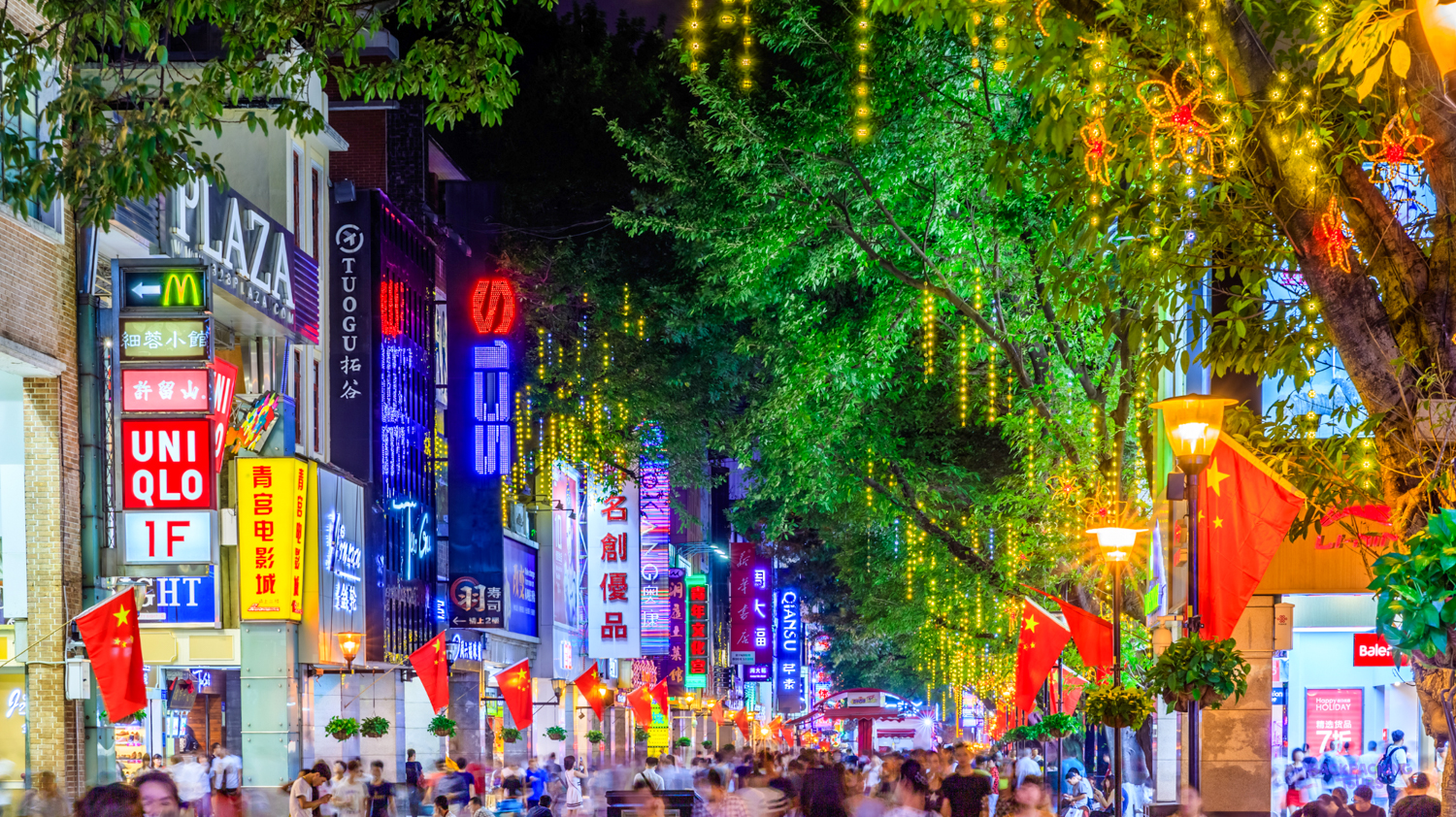 A bustling street in Beijing at night, illuminated by vibrant neon signs and decorative lights.