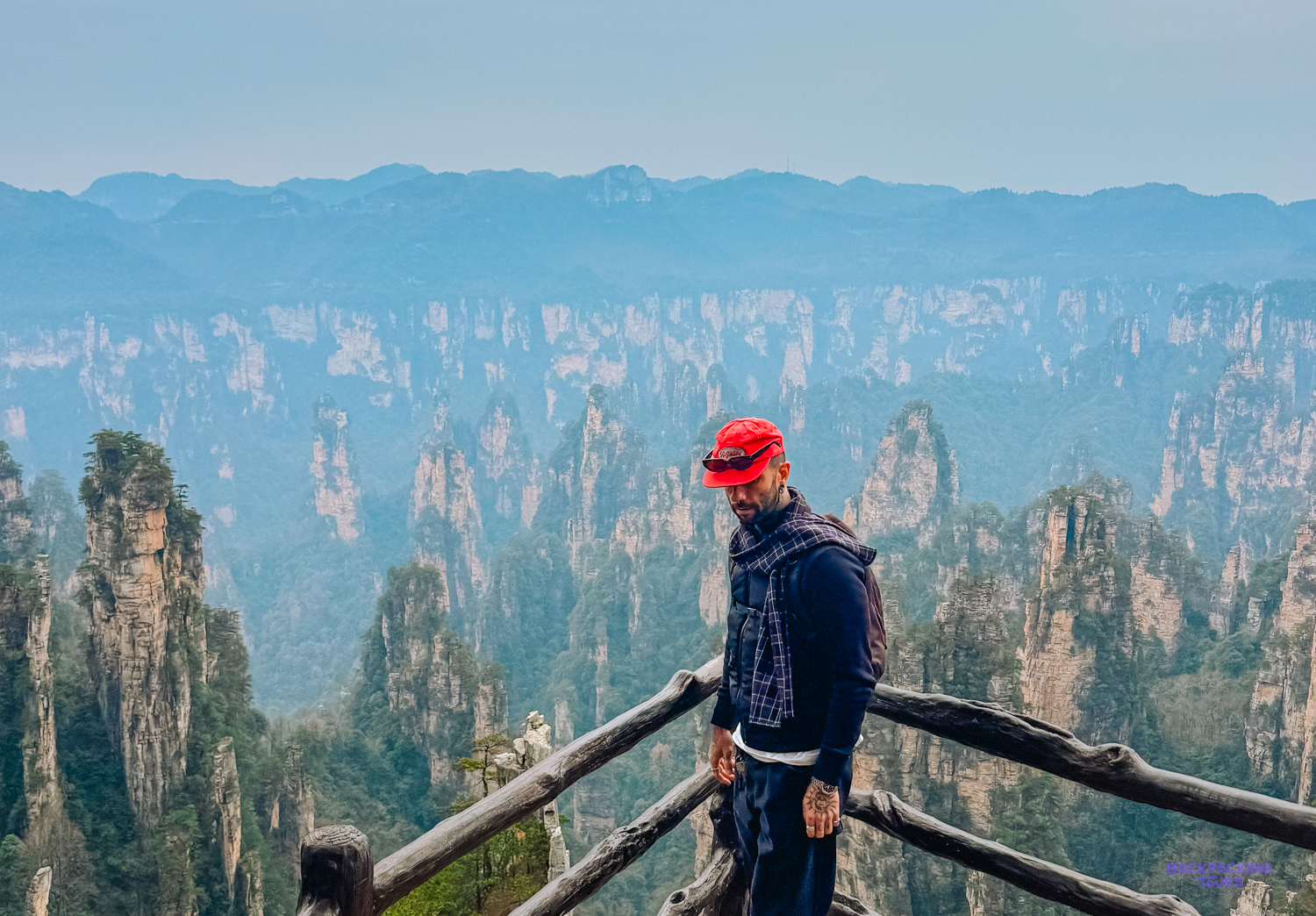 Man in a red cap admiring the breathtaking, misty pillar mountains of Zhangjiajie National Park.