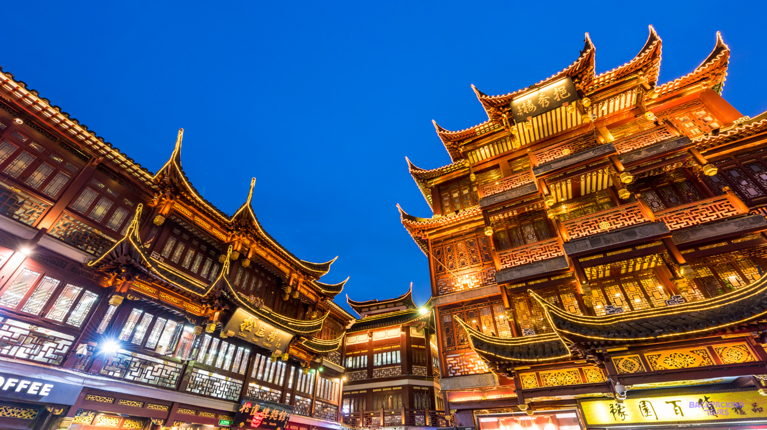 Traditional Chinese buildings with illuminated ornate roofs under a deep blue evening sky in Shanghai.