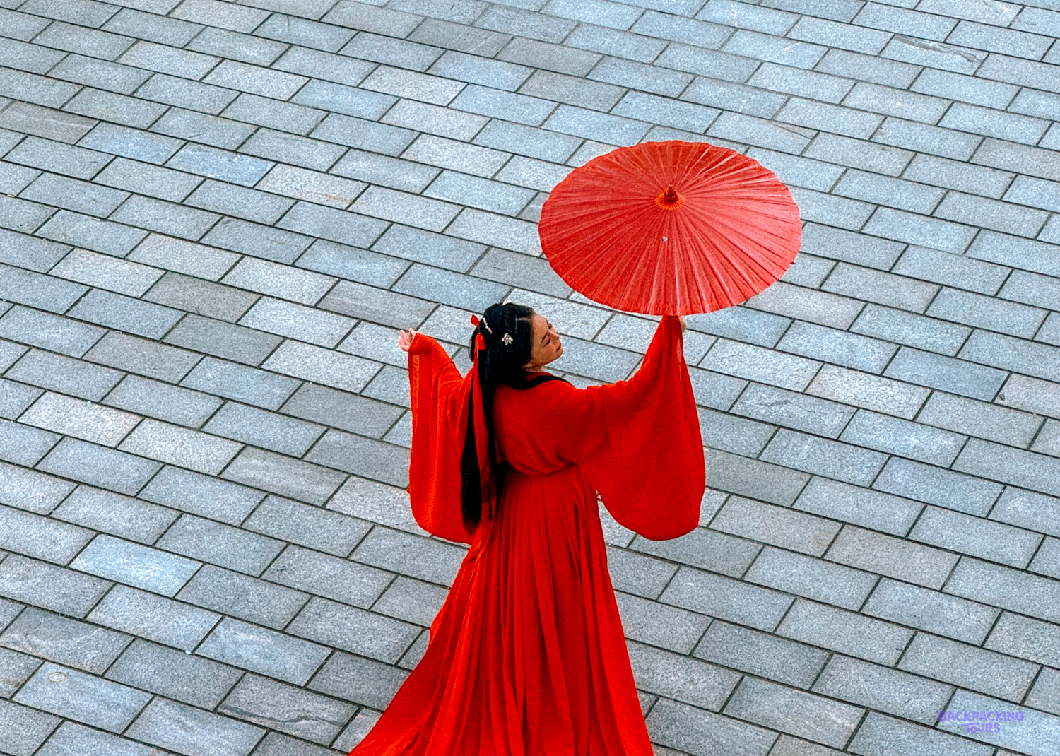 A person in a vibrant red traditional Chinese dress gracefully holds a red parasol aloft in Shanghai.