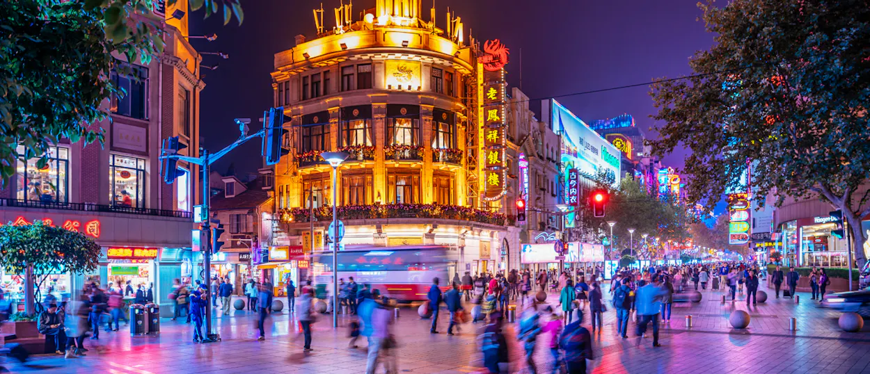 A vibrant Shanghai street at night, with crowds of people and brightly lit buildings.