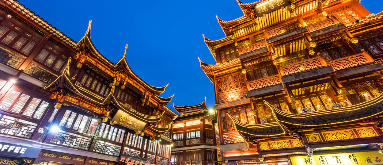 Ornate traditional Chinese buildings with glowing lights under a deep blue evening sky in Shanghai.