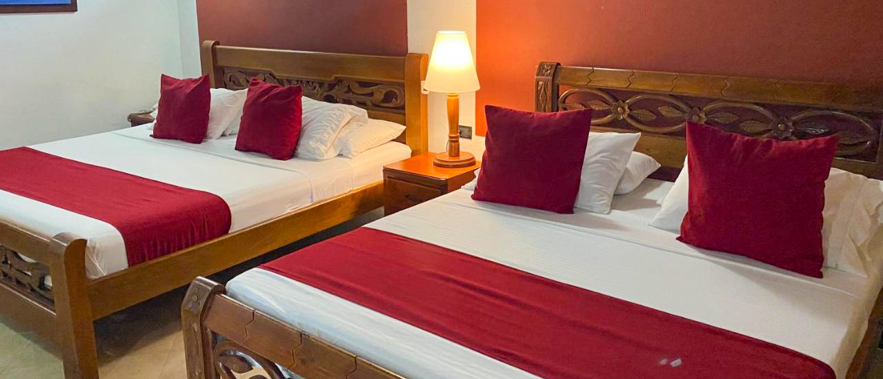 Two comfortable beds with white linens and red accents in a hotel room in Cartagena.