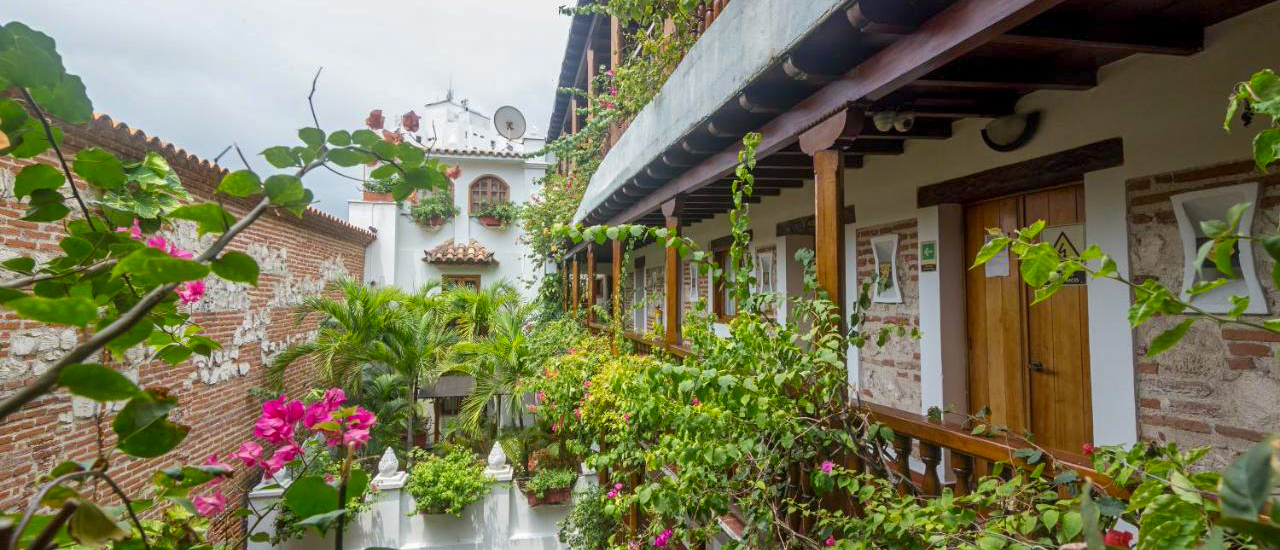 A vibrant courtyard in Cartagena with lush green plants, pink flowers, and historic colonial architecture.