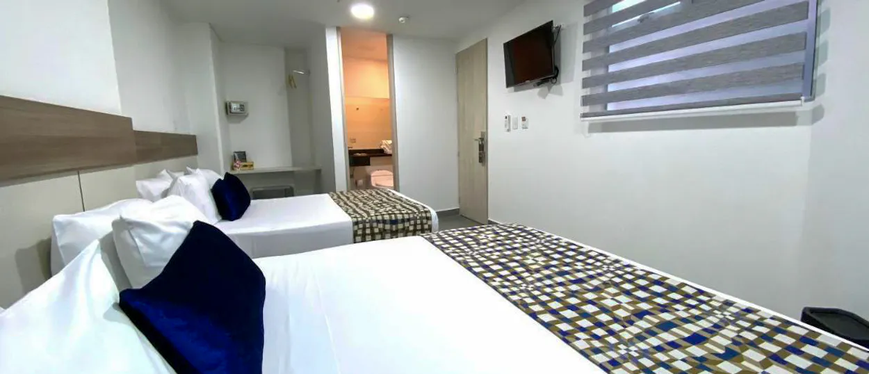 A clean and modern hotel room in Medellin with two beds, white linens, and a TV.
