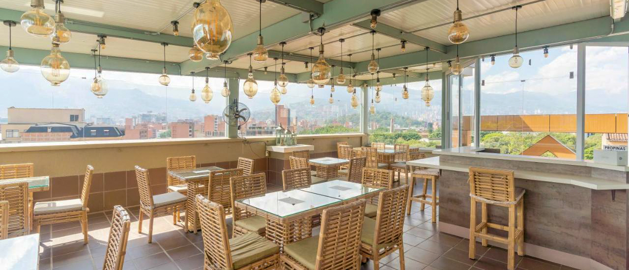 Relaxing rooftop bar in Medellin with many hanging lights, wicker furniture, and a mountain city backdrop.