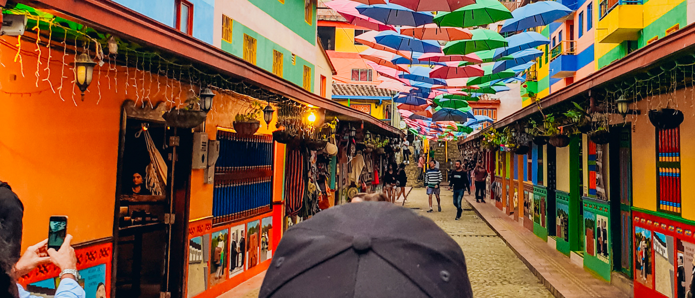 A vibrant street in Cartagena with colorful buildings, suspended umbrellas, and people exploring.