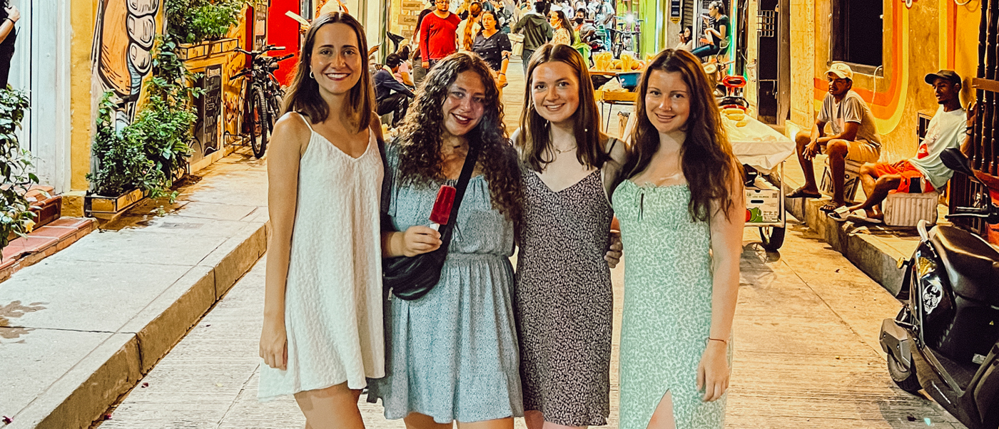 Four happy women pose on a vibrant, colorful street in Cartagena at night.