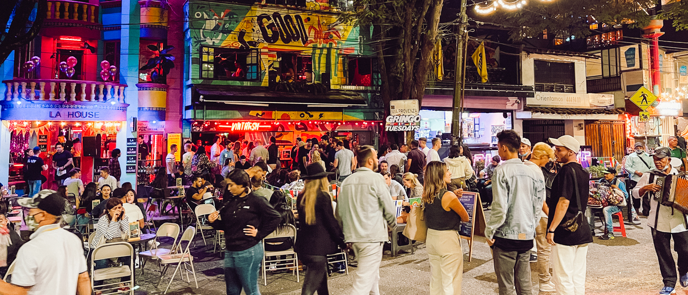 Travelers and locals enjoy a festive night with music and drinks on a colorful street in Medellin.