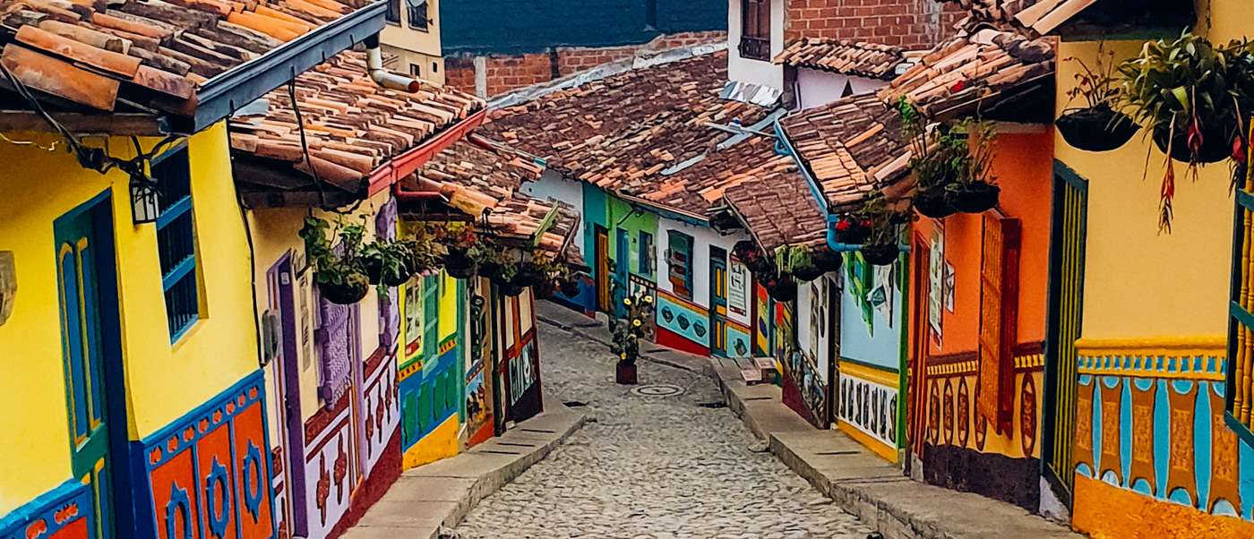 A charming cobblestone street in Guatape, Colombia, lined with vibrant, intricately painted houses and hanging plants.