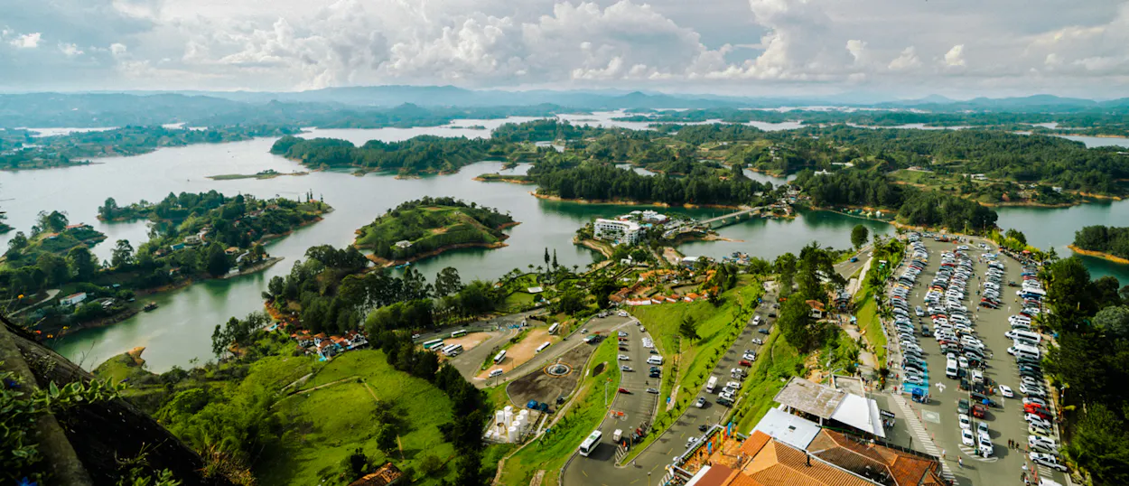 Panoramic view of Guatape's sprawling lakes, lush green islands, and a busy parking lot.