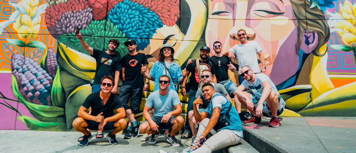 A group of happy male travelers posing in front of a vibrant street art mural in Medellin.