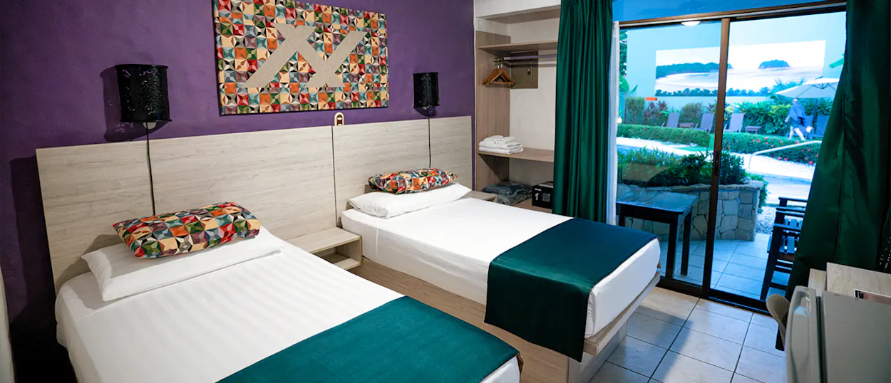 A colorful hotel room with two single beds and a patio overlooking a garden in Samara.