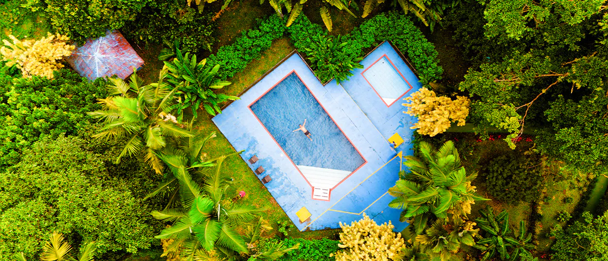 Aerial view of a person floating in a blue swimming pool surrounded by lush tropical greenery in Costa Rica.