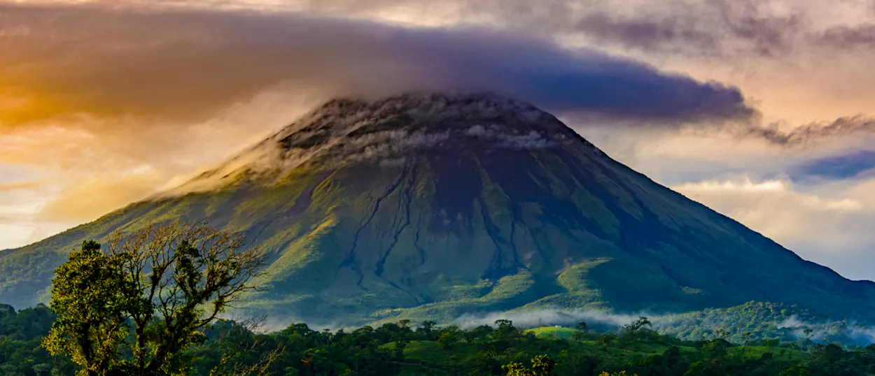 Majestic Arenal Volcano with its peak shrouded in clouds, surrounded by lush Costa Rican rainforest.