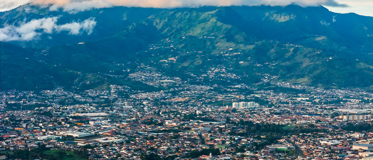 An expansive view of San Jos es city nestled against lush green mountains under a cloudy sky.