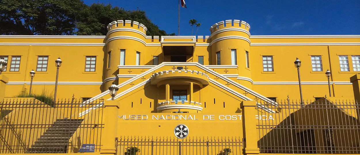 Vibrant yellow National Museum of Costa Rica building with fortress-like towers under a blue sky in San José.