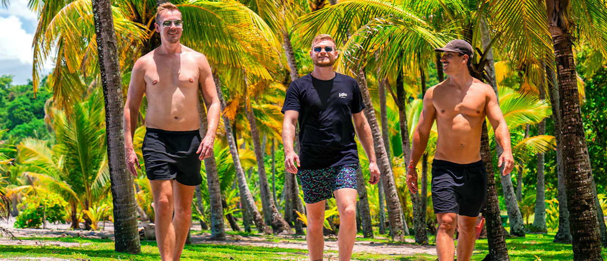 Three men walk happily through a sunny palm grove on a tropical beach day in Costa Rica.
