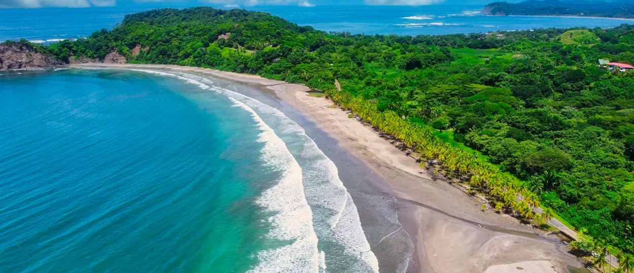 Waves crash on a beautiful tropical beach bordered by lush green jungle in Guanacaste, Costa Rica.