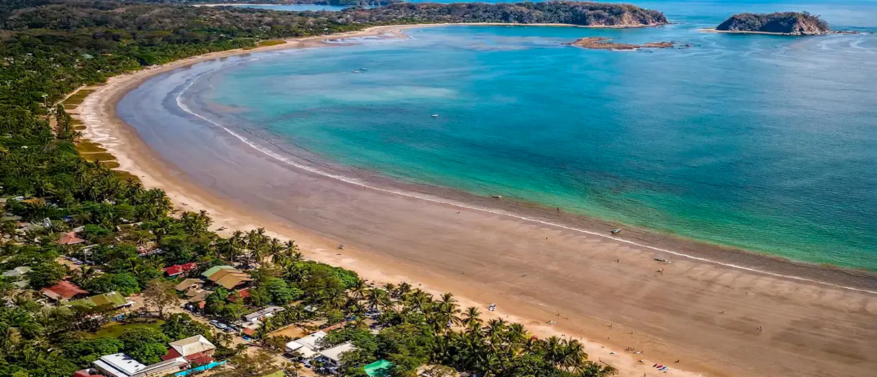 Samara, Costa Rica, features a wide crescent beach, clear turquoise ocean, and lush tropical vegetation.