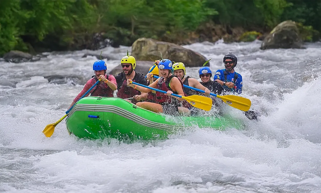 Six adventurers in a green raft navigate thrilling white-water rapids surrounded by lush Costa Rican rainforest.