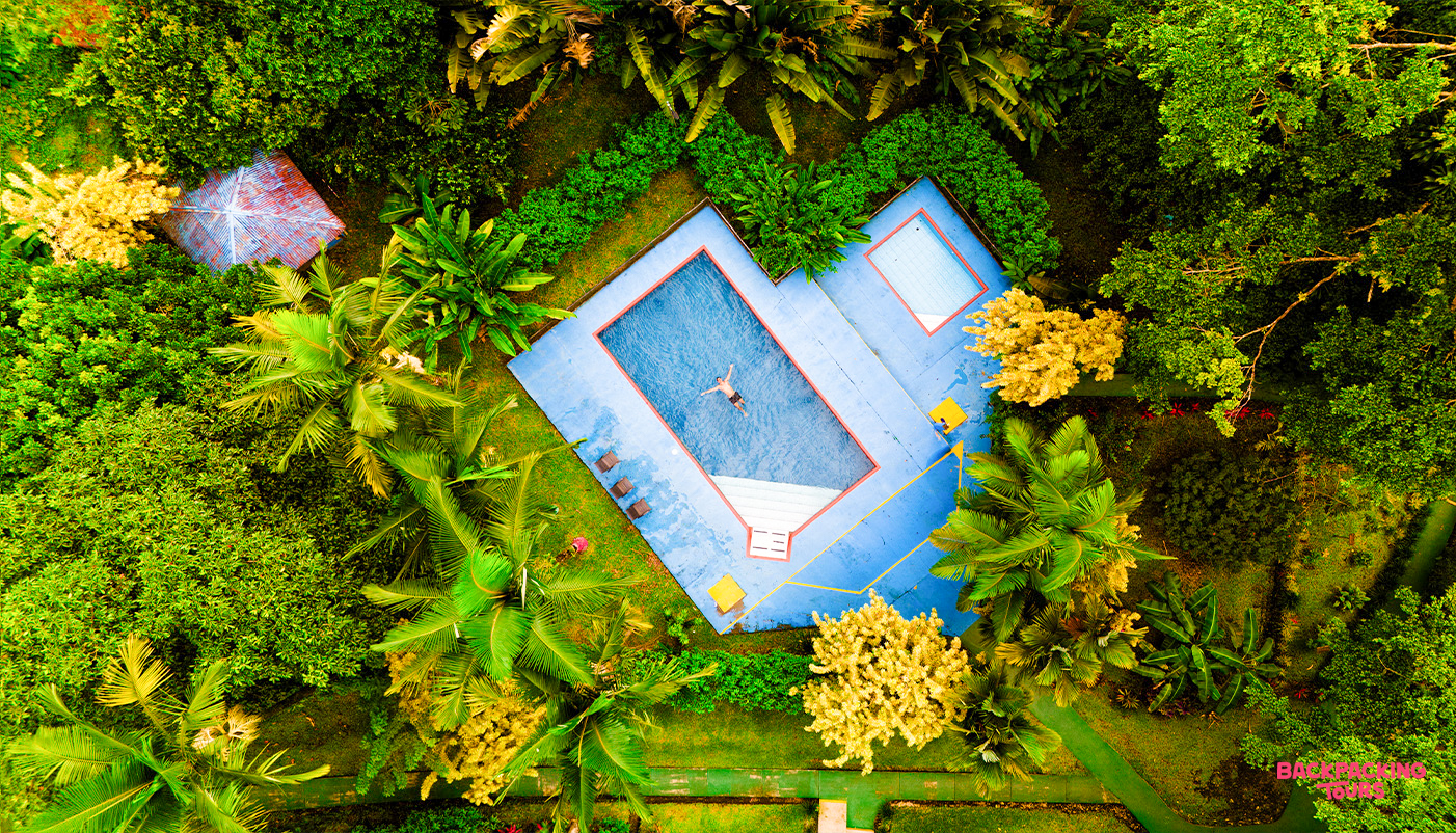 A person floats in a bright blue resort pool, surrounded by lush tropical greenery in La Fortuna.