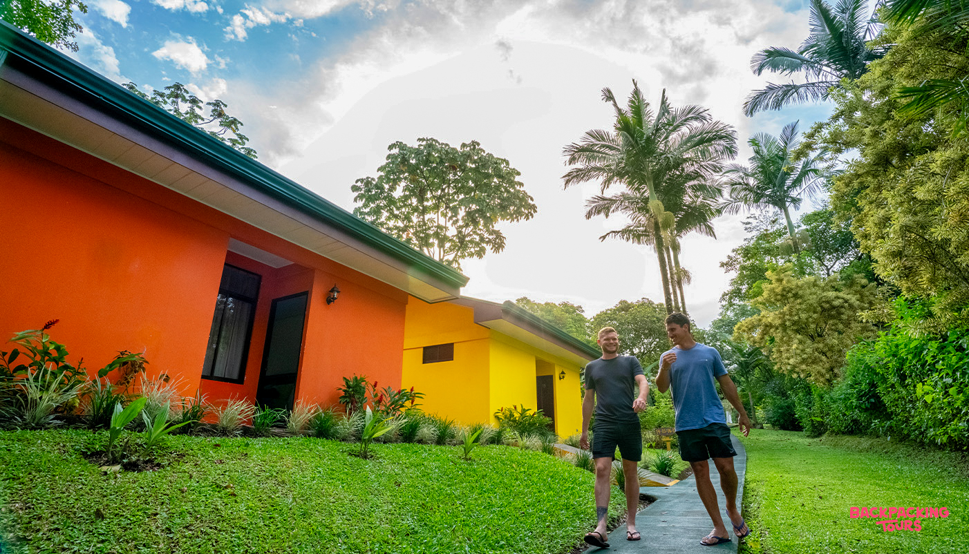Two happy men walk on a path between colorful buildings at a tropical resort in La Fortuna.