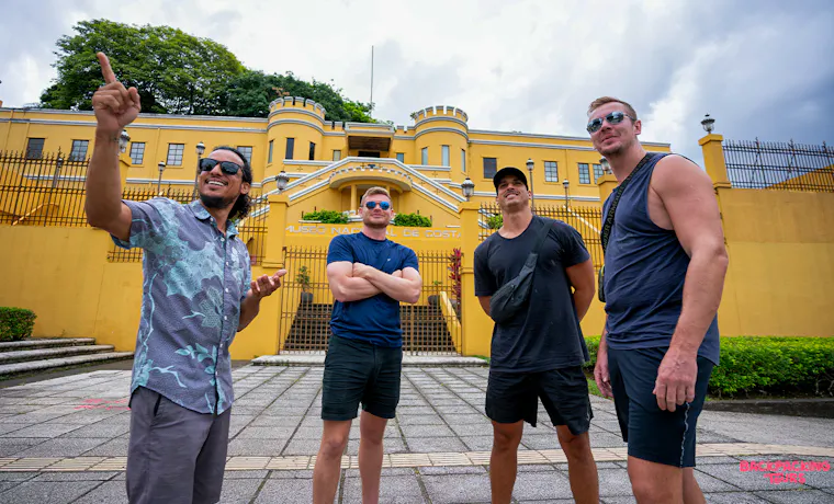 Four men on a guided city tour in San Jos es, pointing at a vibrant yellow historic building.