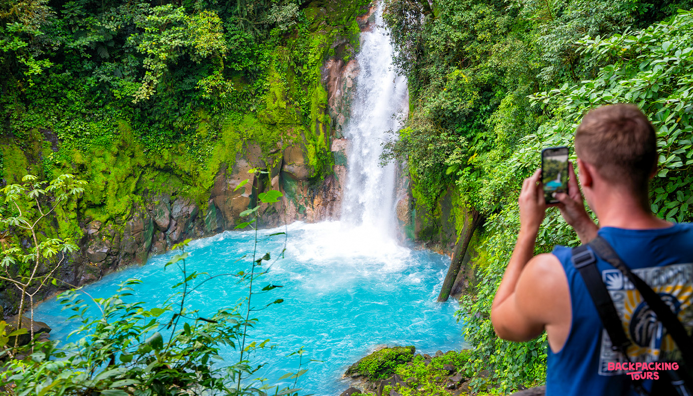 A visitor photographs the vibrant blue waters of a stunning waterfall in the Costa Rican rainforest.