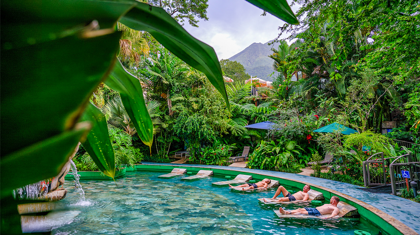 Guests relaxing in a lush tropical thermal pool with a majestic volcano in Costa Rica.