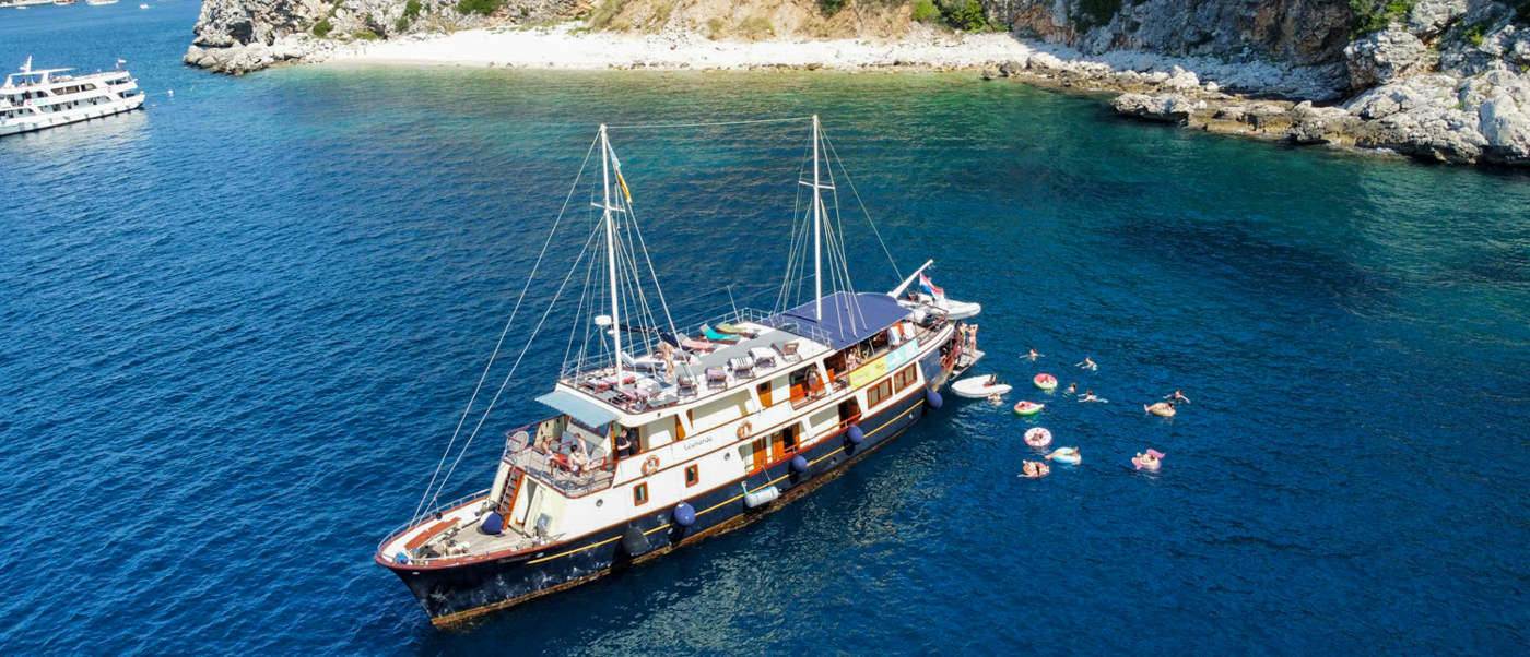 People swim and float on inflatables beside a large sailing boat during a swim stop in Makarska.