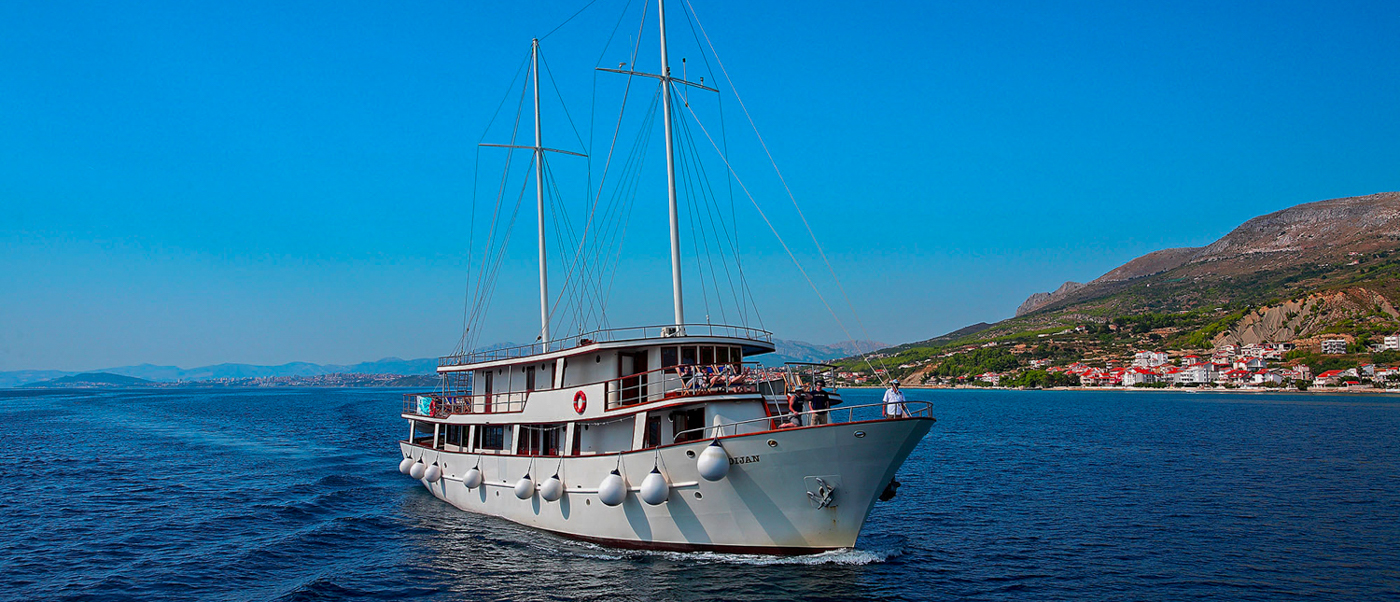 A white sailing vessel glides across the calm sea towards the scenic coast of Mljet, Croatia.