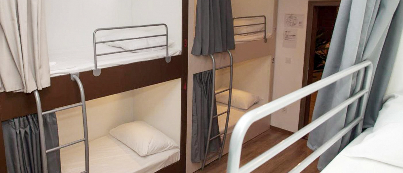 A clean and inviting hostel dorm room with multiple bunk beds, each with privacy curtains, in Split.