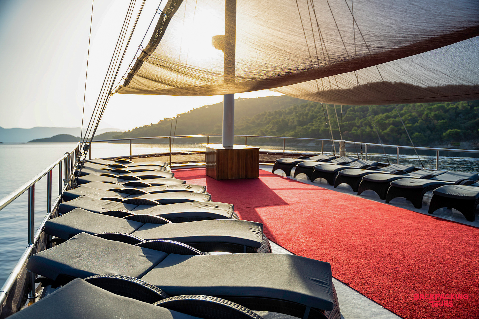 Spacious sun deck of a premium sailing boat with lounge chairs under a sail awning at sunset.