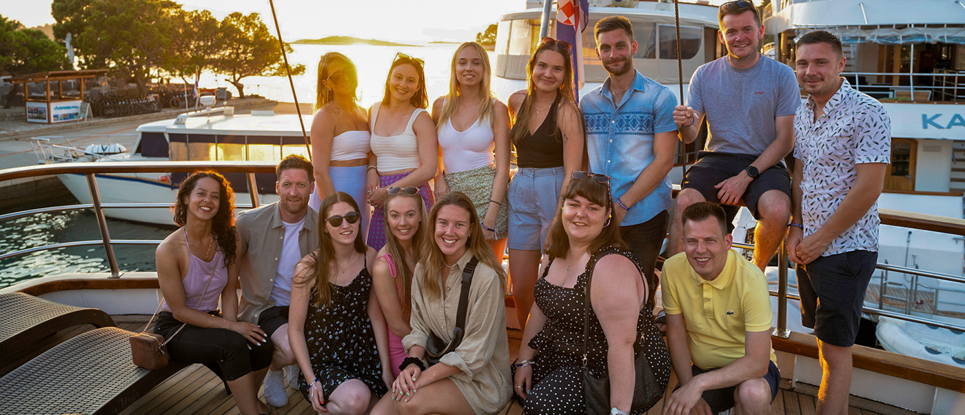 A happy group of young travelers poses on a boat deck at sunset in Korcula, Croatia.