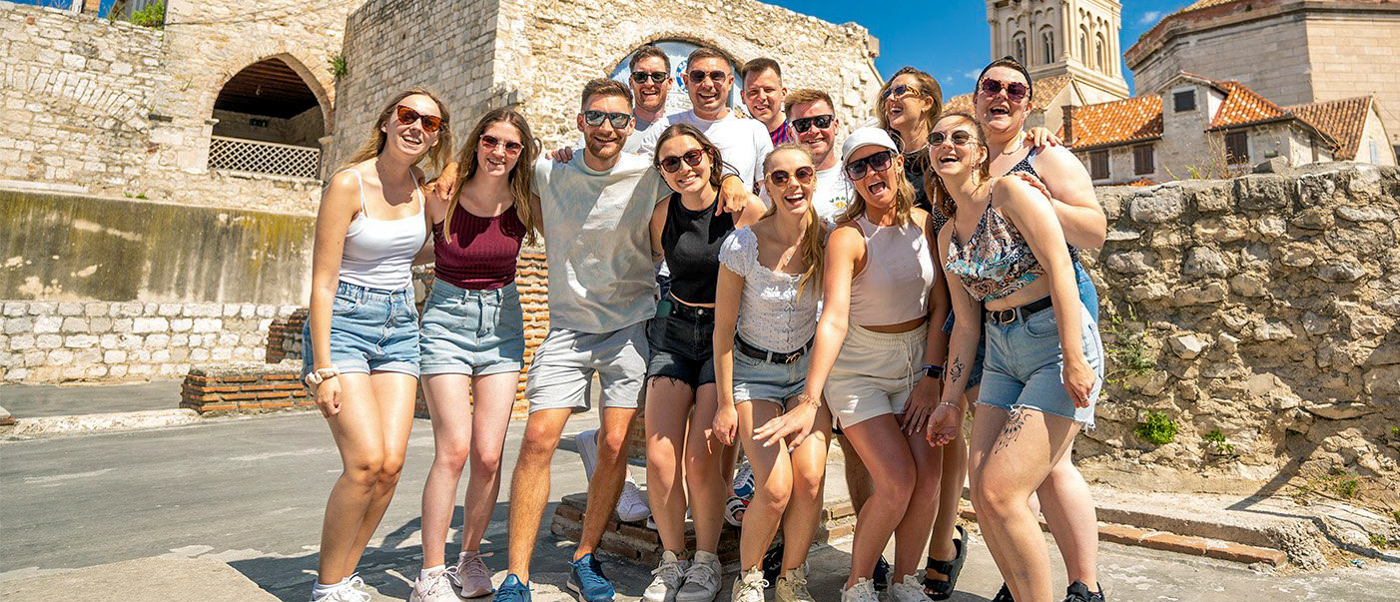 Smiling friends pose for a farewell photo in sunny Split, Croatia, with historic stone buildings.