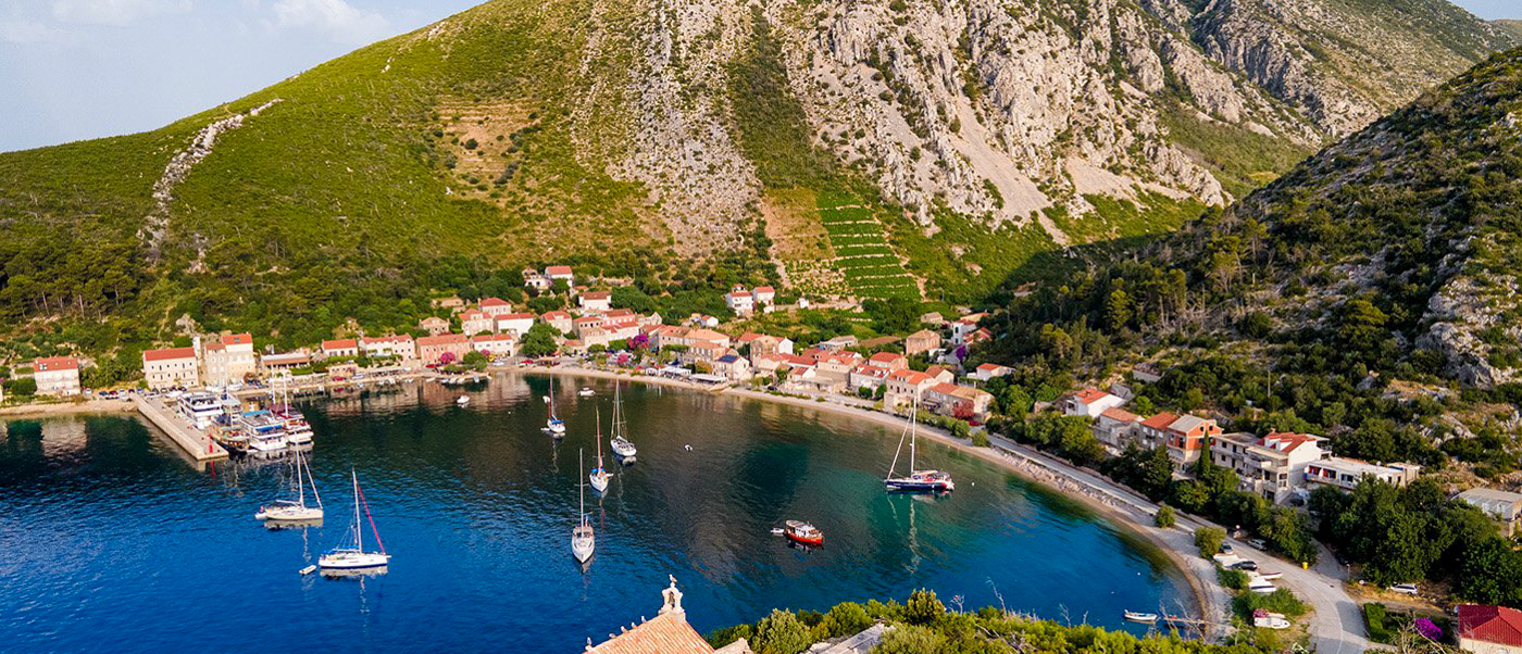 Peaceful Trstenik, Croatia, with sailboats in a calm bay, nestled beneath green mountains and vineyards.