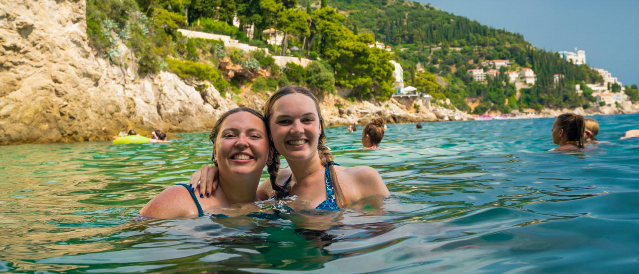 Two young women smiling and swimming in the clear waters of Trstenik, Croatia.