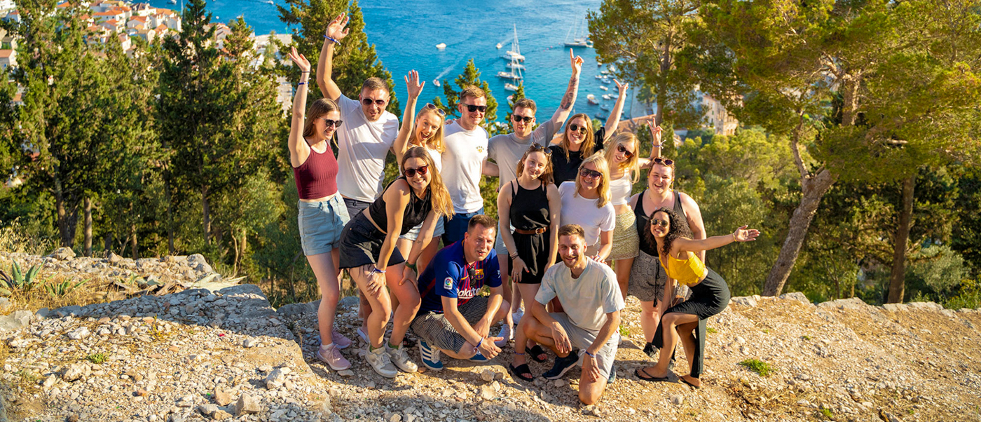 A happy group of young travelers posing on a sunny Hvar viewpoint overlooking the blue Adriatic Sea.