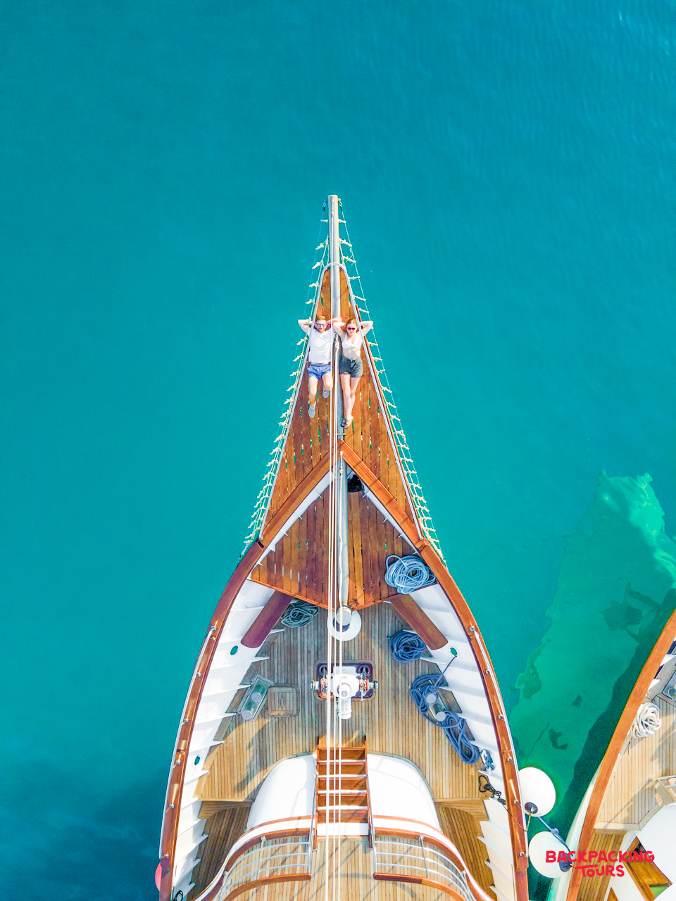 Two people relaxing on a sailing boat, sunbathing in the clear turquoise waters of Makarska.