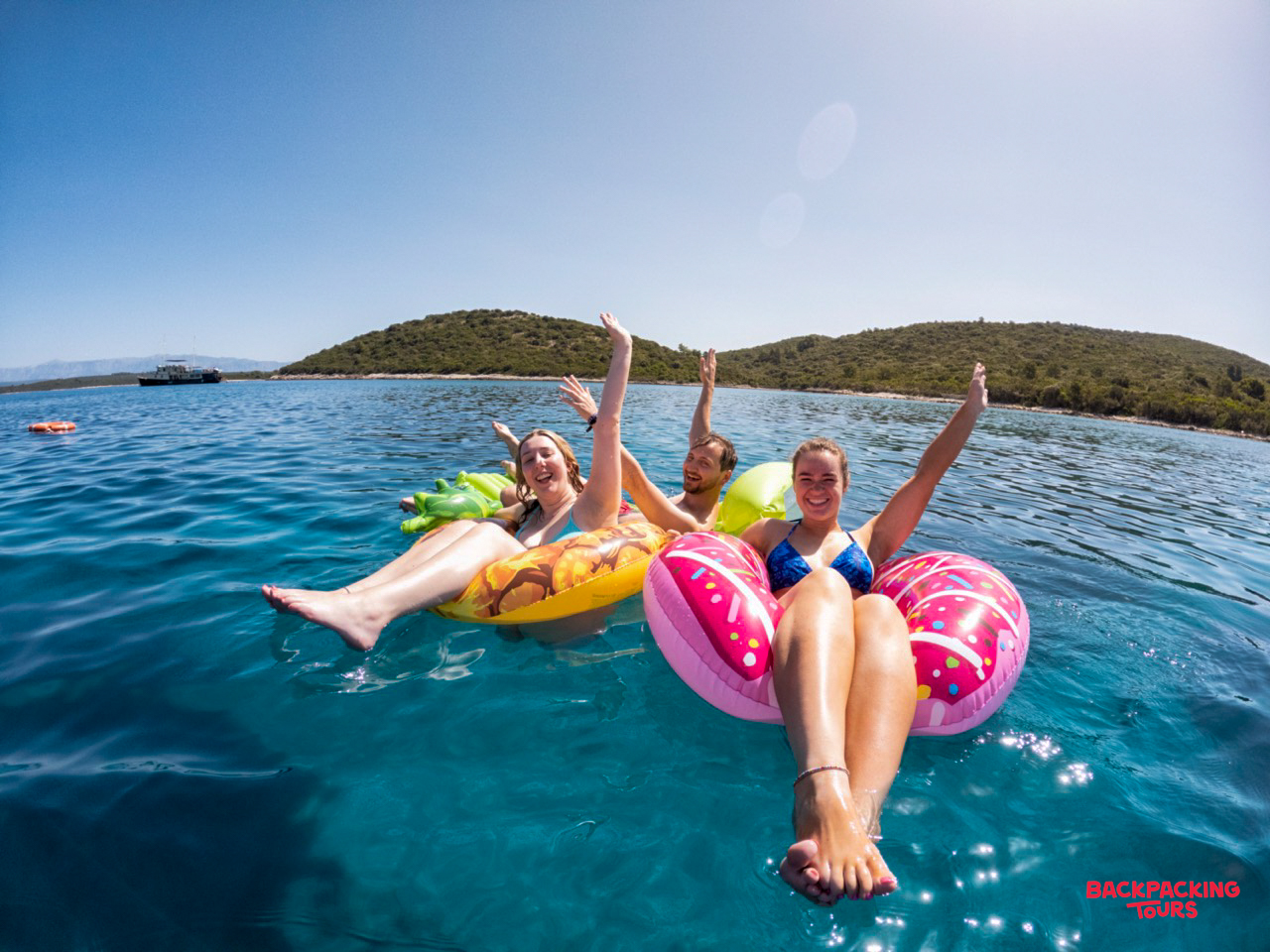 Backpackers enjoy a refreshing swim stop, floating on inflatables in the clear blue sea.