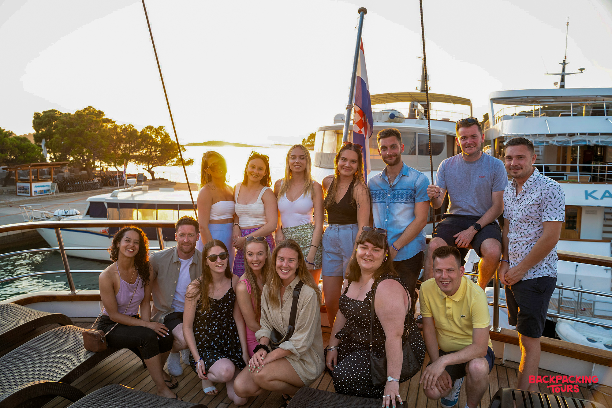 Travelers smile on a boat deck at sunset, cruising into the charming island of Korcula.