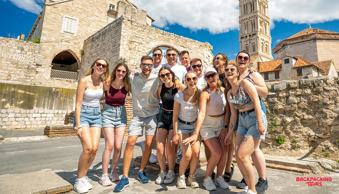 Smiling backpackers gather for a farewell group photo in the historic city of Split, Croatia.