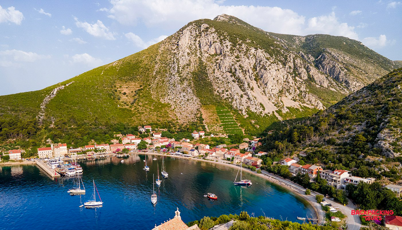 Boats anchored in the clear blue bay of Trstenik, a quiet Croatian village nestled against a green mountain.